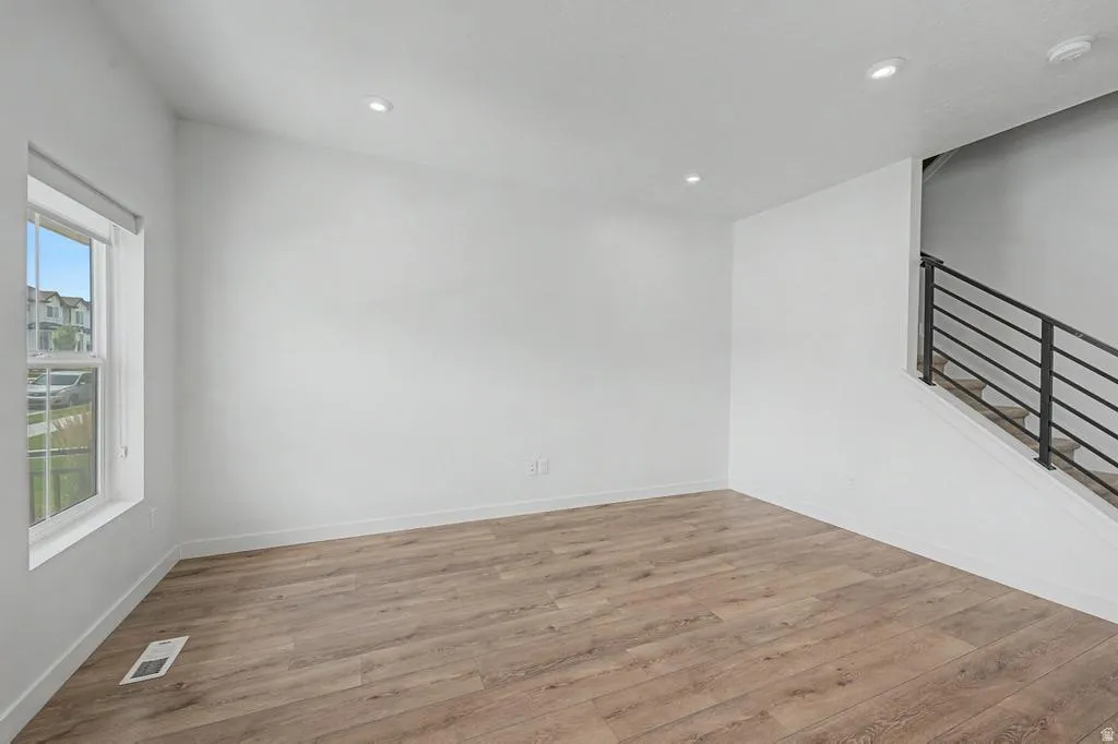 Spacious room featuring wood-finish flooring, recessed lighting, a large window, and a contemporary staircase with metal railings