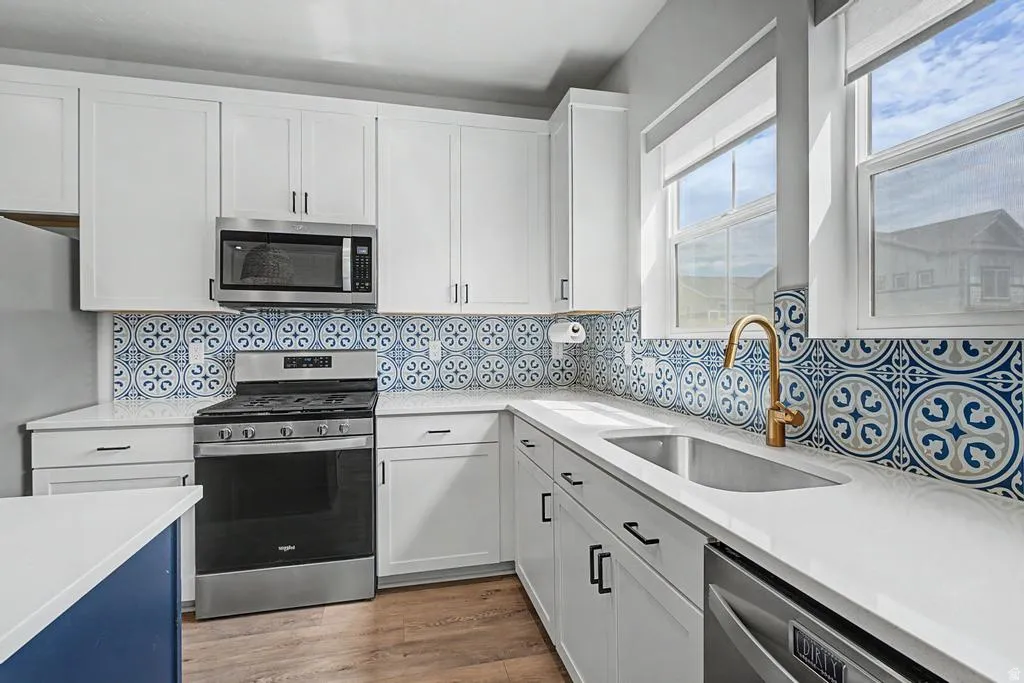 Contemporary kitchen featuring white cabinetry, stainless steel appliances, a patterned tile backsplash, and light-colored countertops