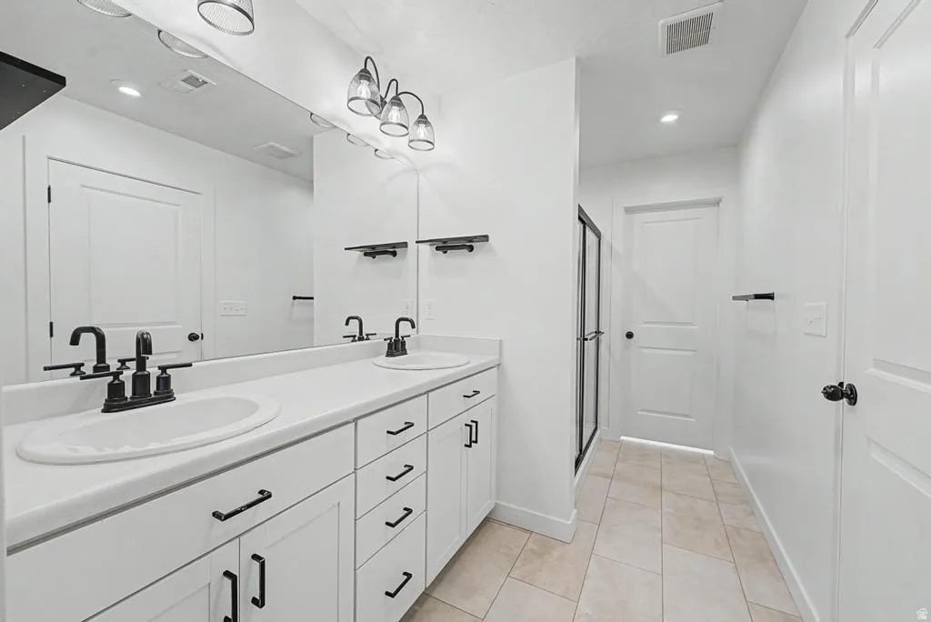 Double vanity with matte black fixtures and hardware, white cabinetry, and a large wall-mounted mirror