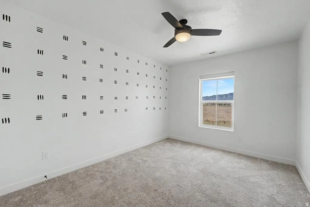 Room featuring light gray carpet flooring, a single window with a mountain backdrop, a ceiling fan with integrated lighting, and a white wall with a geometric pattern