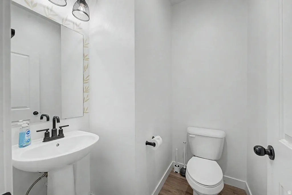 Pedestal sink with matte black faucet, wall-mounted mirror, and decorative wallpaper accent