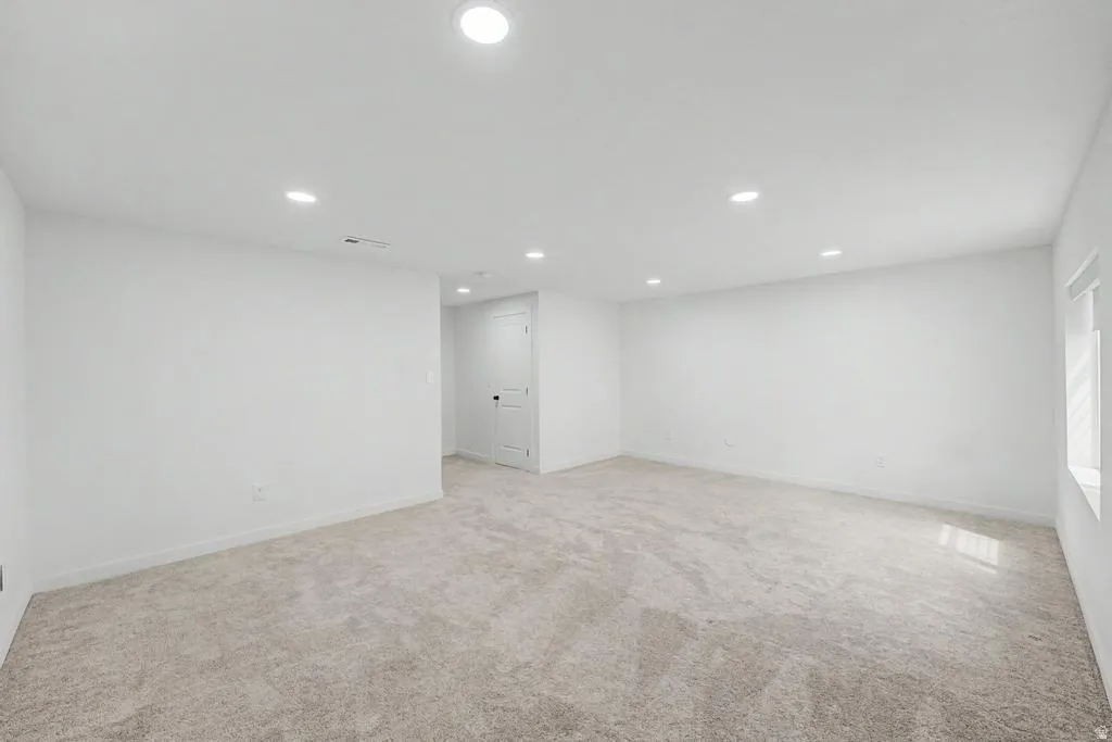 Spacious room with recessed lighting, light-toned carpet flooring, white walls, and a single window offering ambient light
