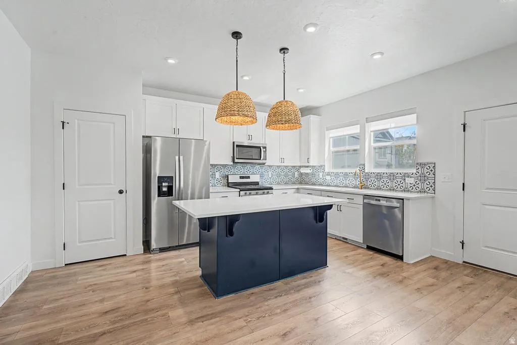 Kitchen featuring a central island with a white countertop and blue base, stainless steel appliances, patterned backsplash, wood-finish flooring, and recessed lighting