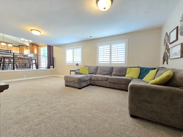 Carpeted living area featuring two windows with plantation shutters, a partial wall with metal railing, and recessed ceiling lighting