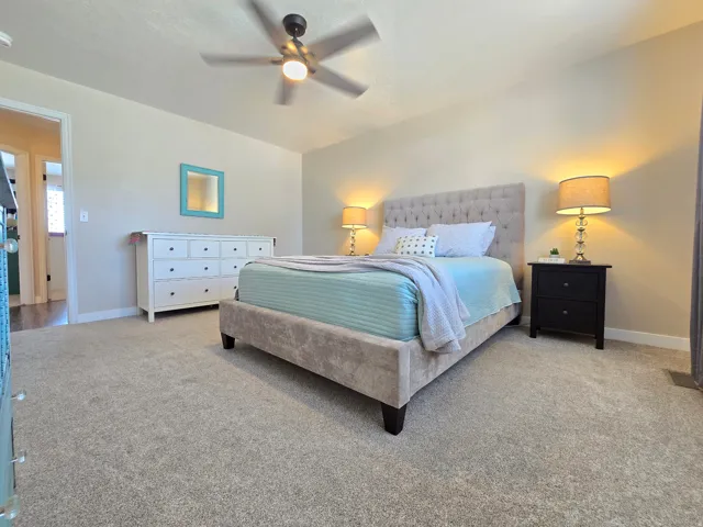 Carpeted bedroom featuring a ceiling fan, light-toned walls, and white baseboards