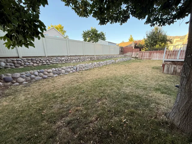 Expansive backyard featuring tiered river rock retaining walls, a full vinyl privacy fence, and a wooden deck