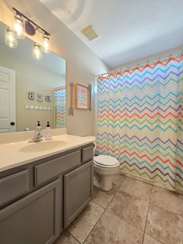 Bathroom featuring a vanity with a white countertop and gray cabinetry, ceramic tile flooring, a built-in toilet, and a shower area