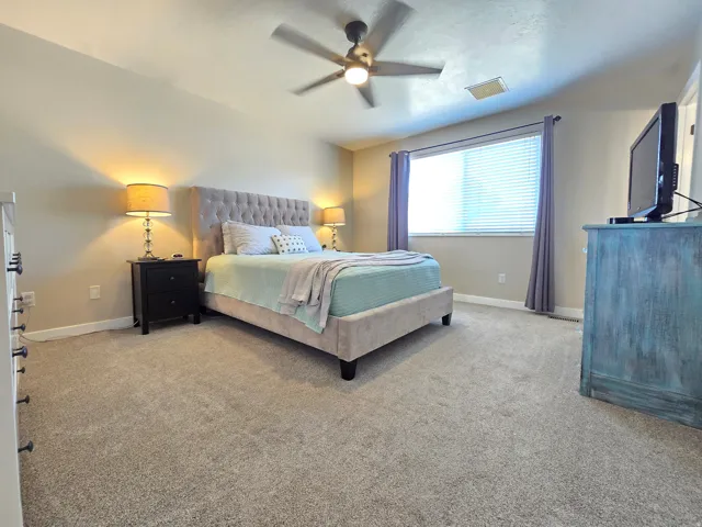 Carpeted bedroom featuring a ceiling fan with integrated lighting, a window with horizontal blinds and drapery, and neutral wall tones