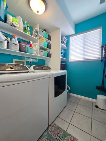 Dedicated laundry space featuring a window, built-in shelving, overhead lighting, and tile flooring