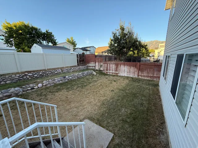 Expansive backyard featuring a tiered rock retaining wall, wood fencing, and vinyl fencing
