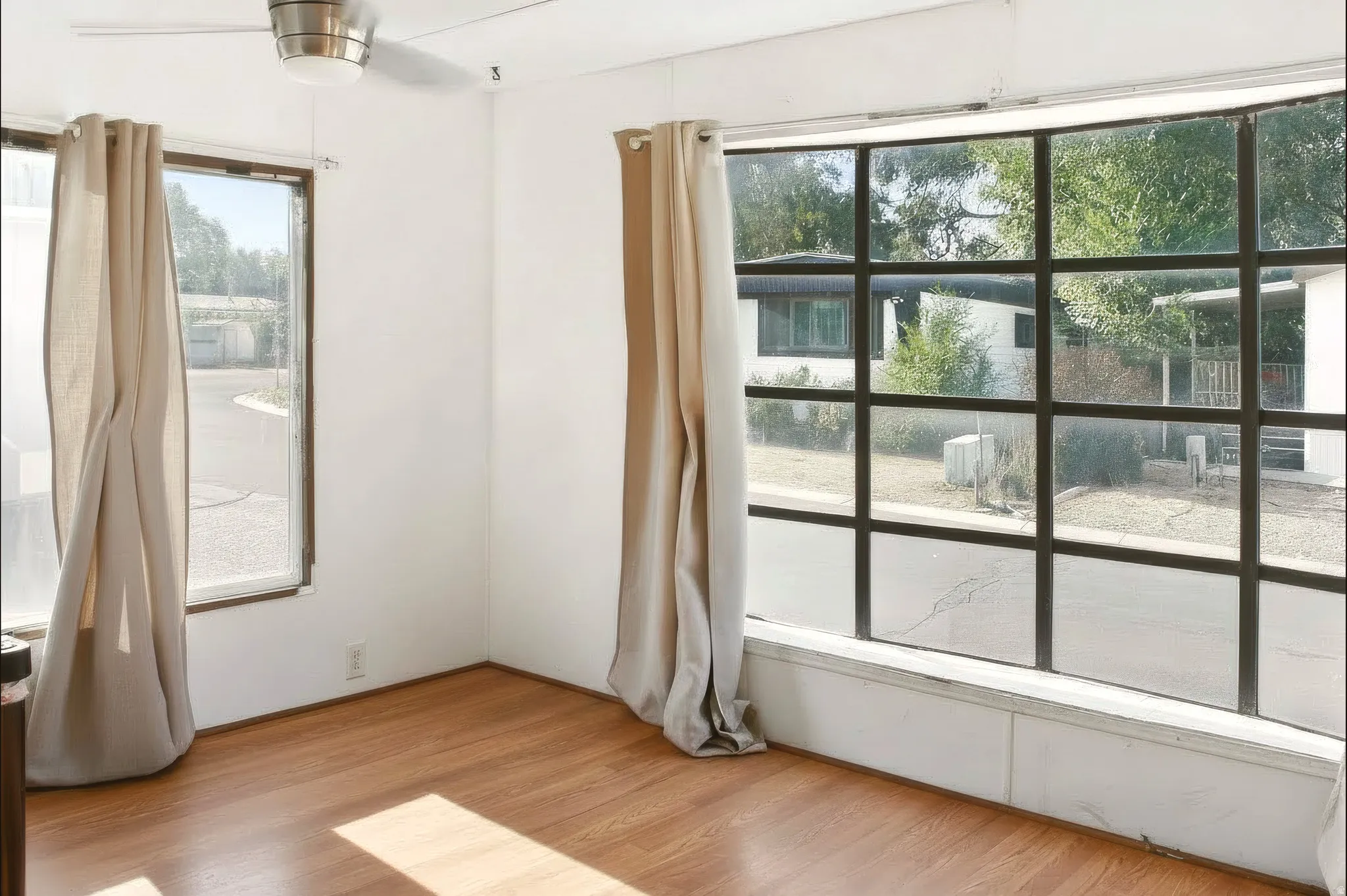Room featuring a prominent bay window with dark muntins, light wood-finish flooring, and a ceiling fan with integrated lighting