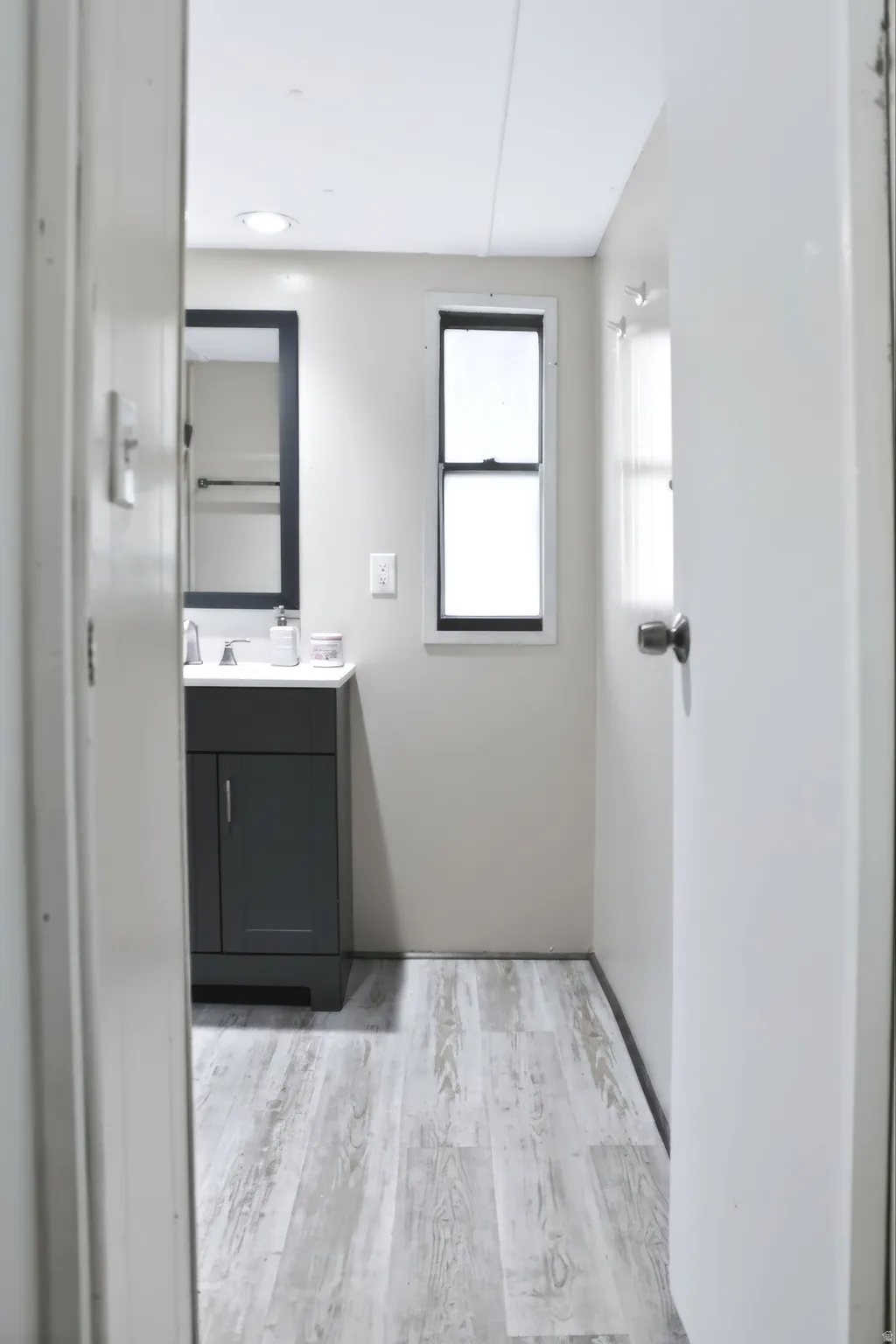 Contemporary bathroom featuring wood-finish flooring, a dark gray vanity with a white countertop, and a rectangular window with dark framing