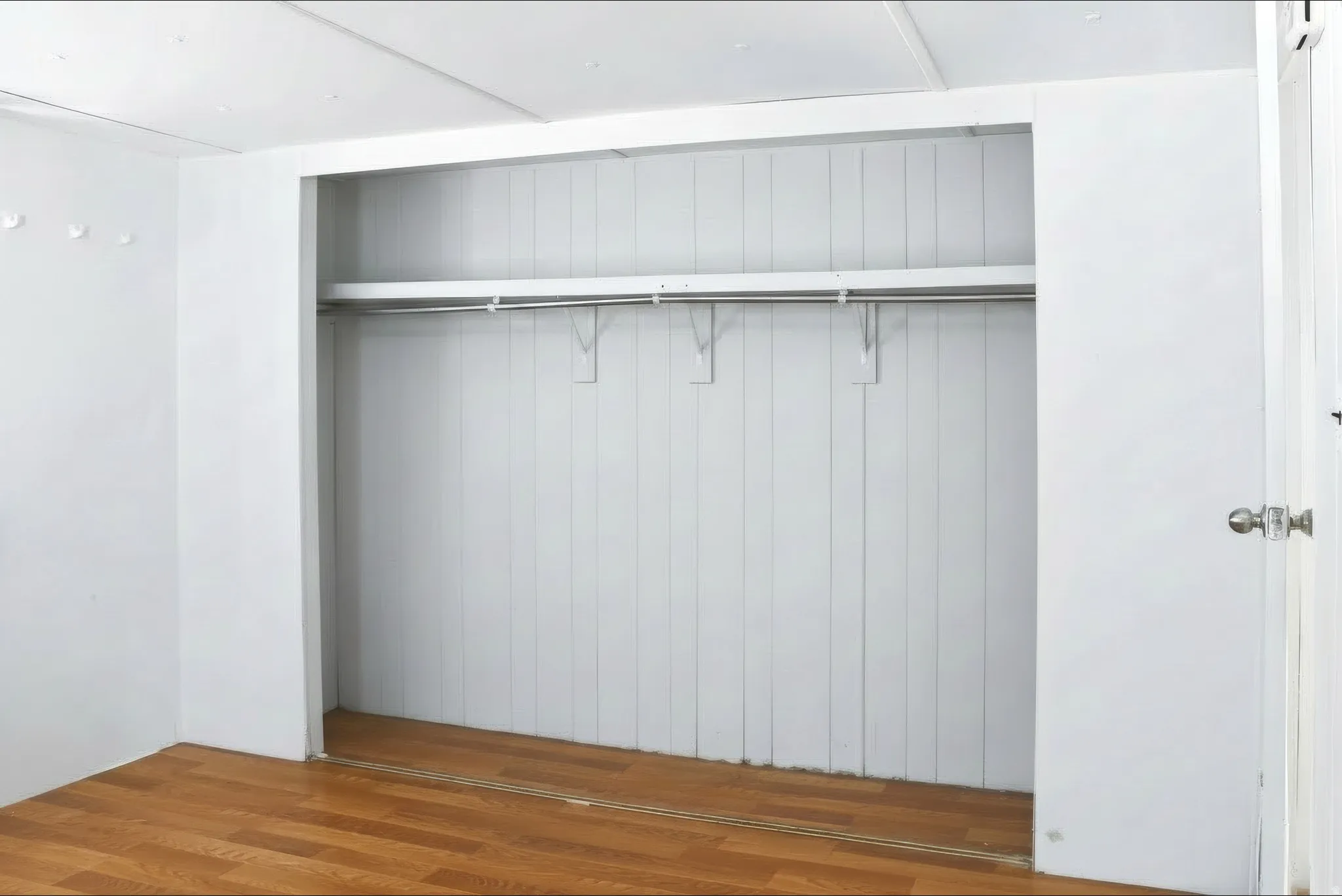 Recessed closet with a single hanging rod, integrated shelving, and wood-finish flooring