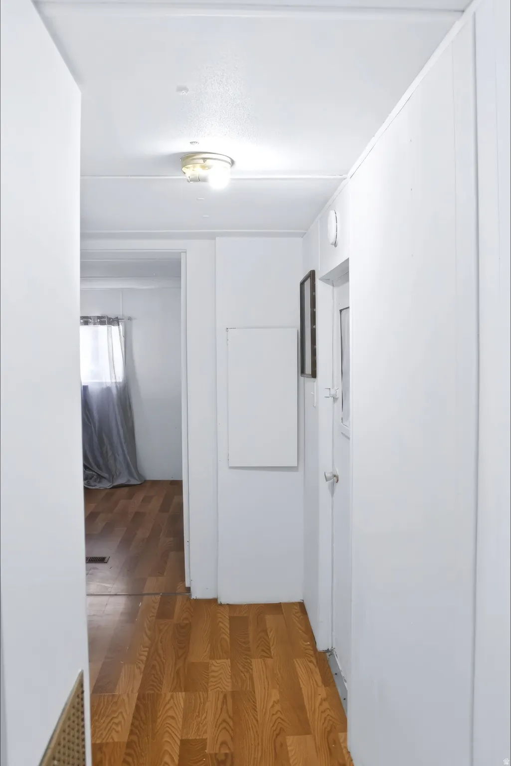 Hallway featuring wood-finish flooring, white paneling, and a flush-mount ceiling light fixture