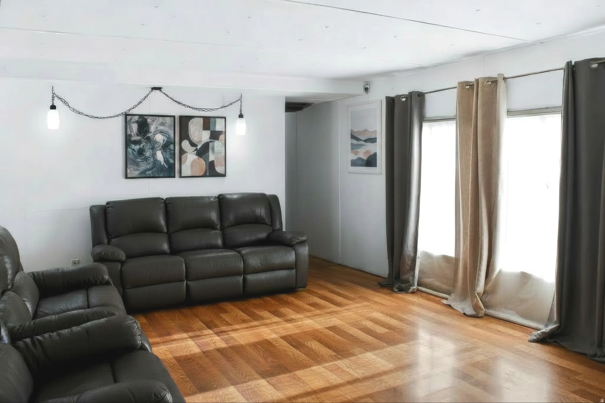 Spacious living area featuring wood-finish flooring, white walls, and a multi-pane window with neutral drapes