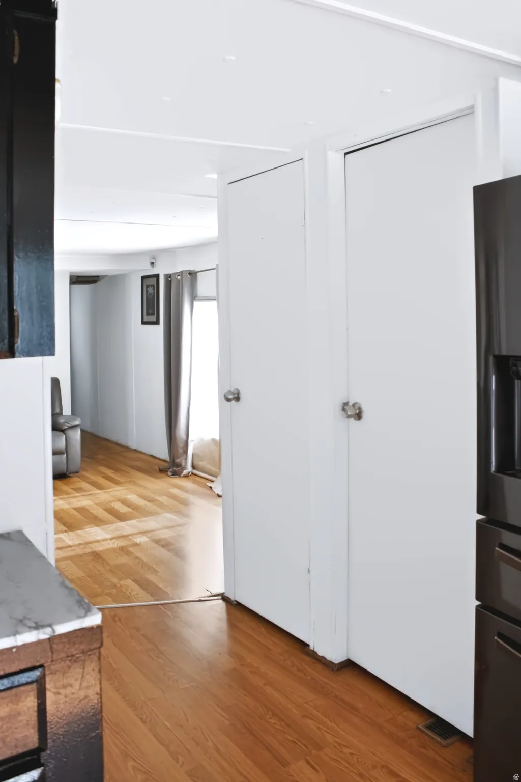 Interior corridor featuring two white doors with round knobs, wood-finish flooring, and a dark built-in refrigerator