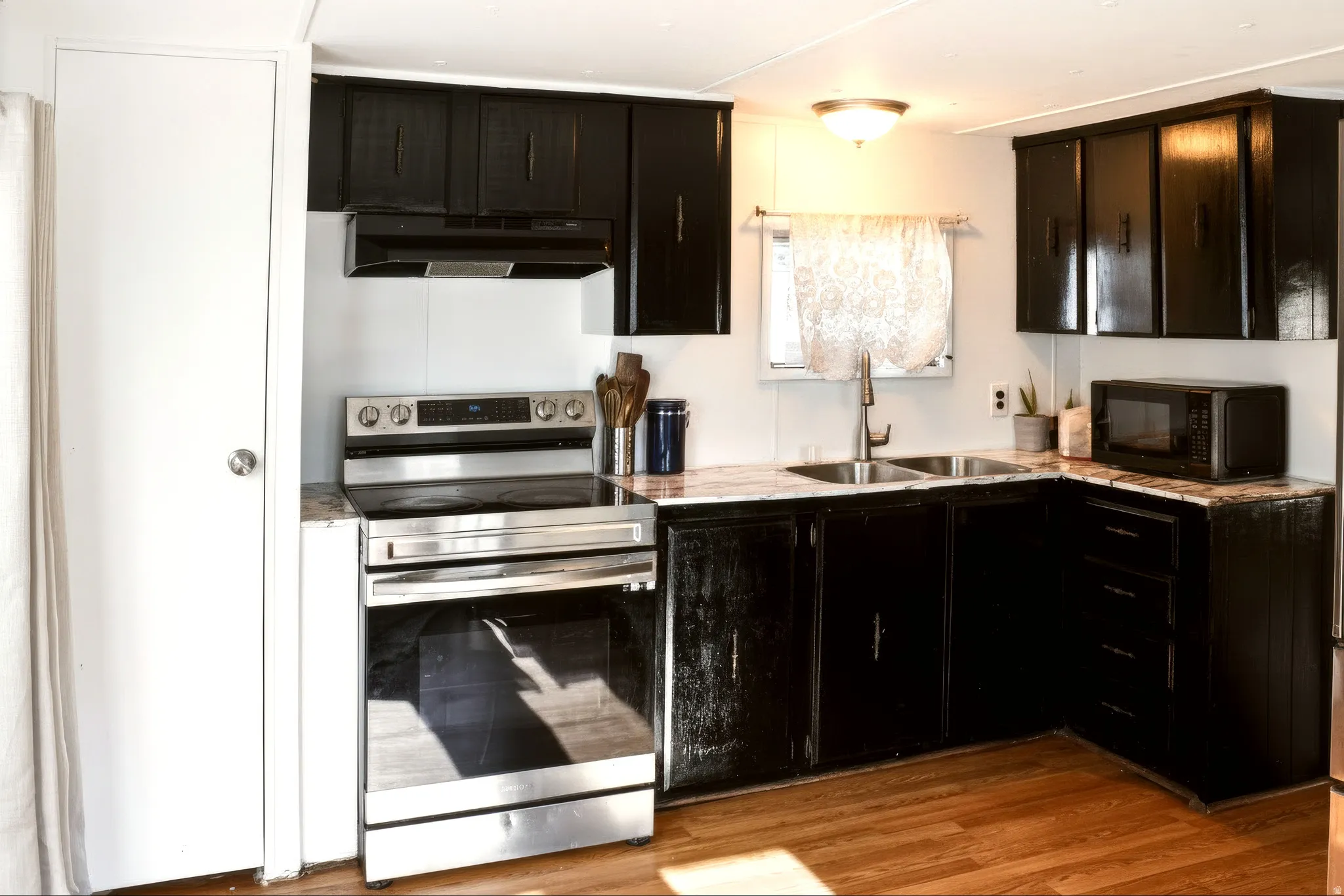 Kitchen featuring black cabinetry, light-toned countertops, a stainless steel electric range, and a double basin sink