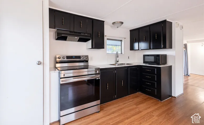 Kitchen featuring black cabinetry, stainless steel range, built-in microwave, and wood-finish flooring