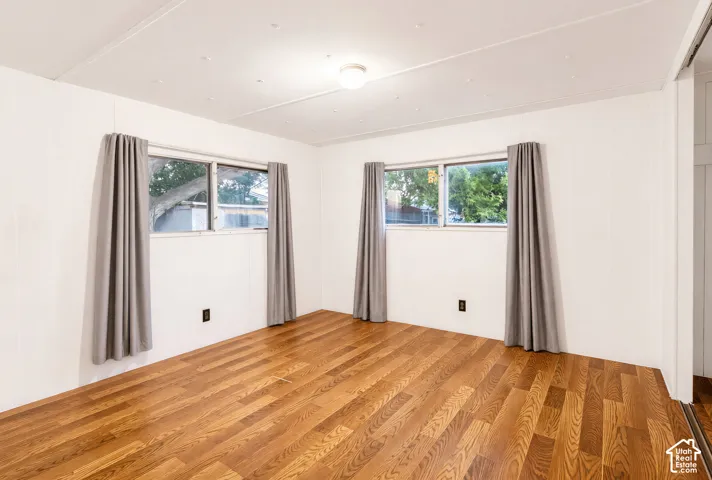Wood-finish flooring, white paneled walls, and two windows with simple drapes