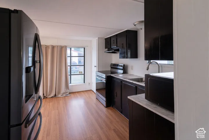 Kitchen featuring dark cabinetry, light-toned countertops, a stainless steel sink, and wood-finish flooring