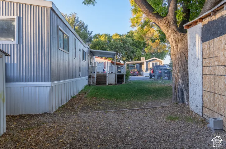 Corrugated metal siding with white trim, a covered porch with steps, and a gravel and grass ground surface