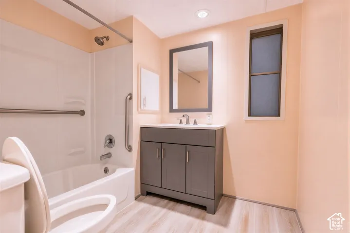 Bathroom featuring a white bathtub, grab bars, a gray vanity with a white countertop, a framed mirror, and wood-finish flooring