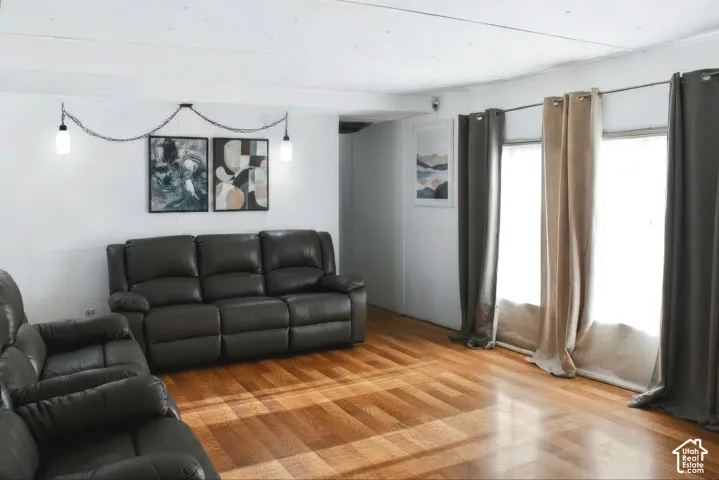 Spacious living area featuring wood-finish flooring, white walls, and a multi-pane window with neutral drapes