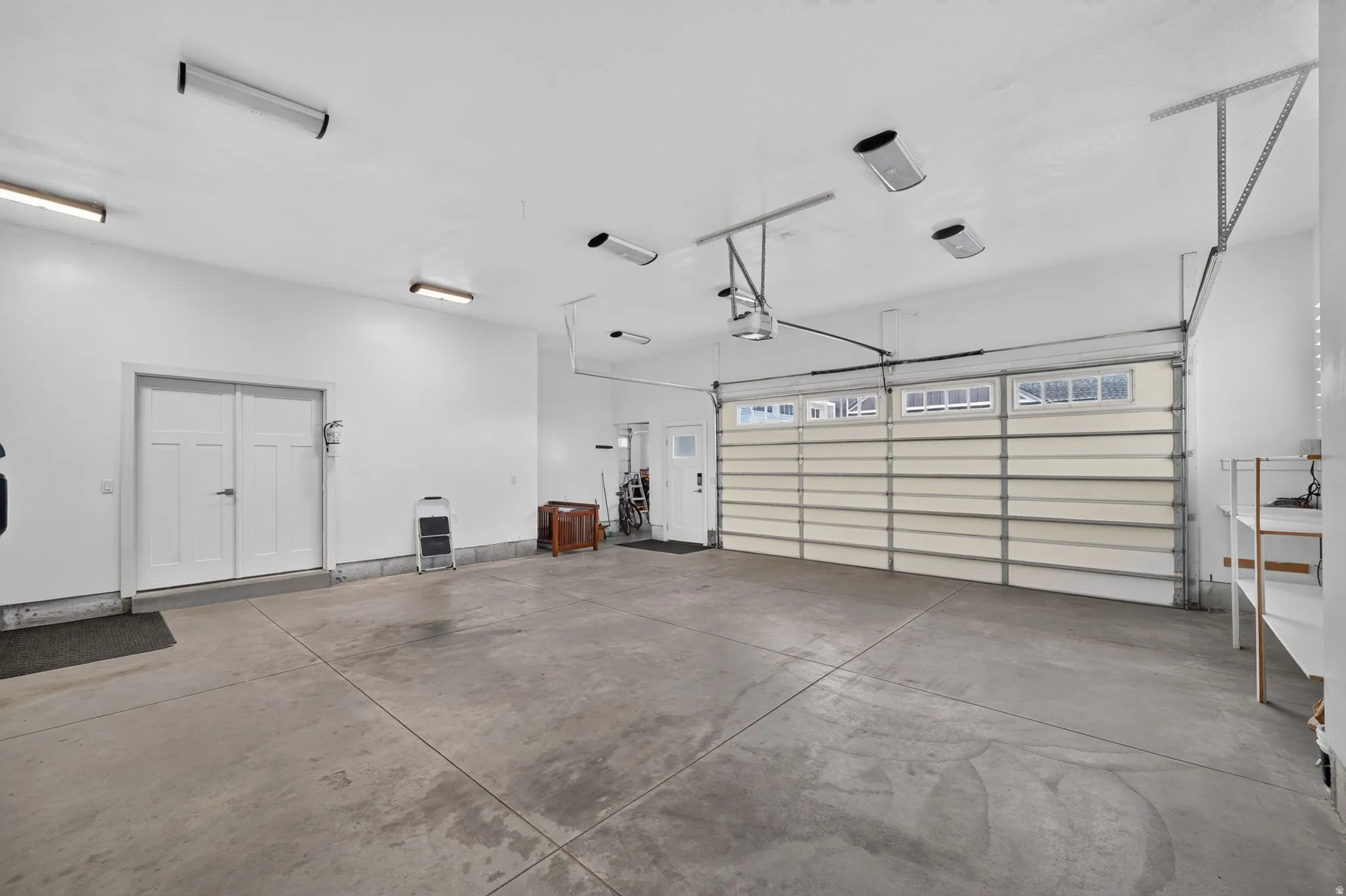 Spacious garage featuring a concrete floor, bright overhead lighting, and a roll-up garage door with transom windows