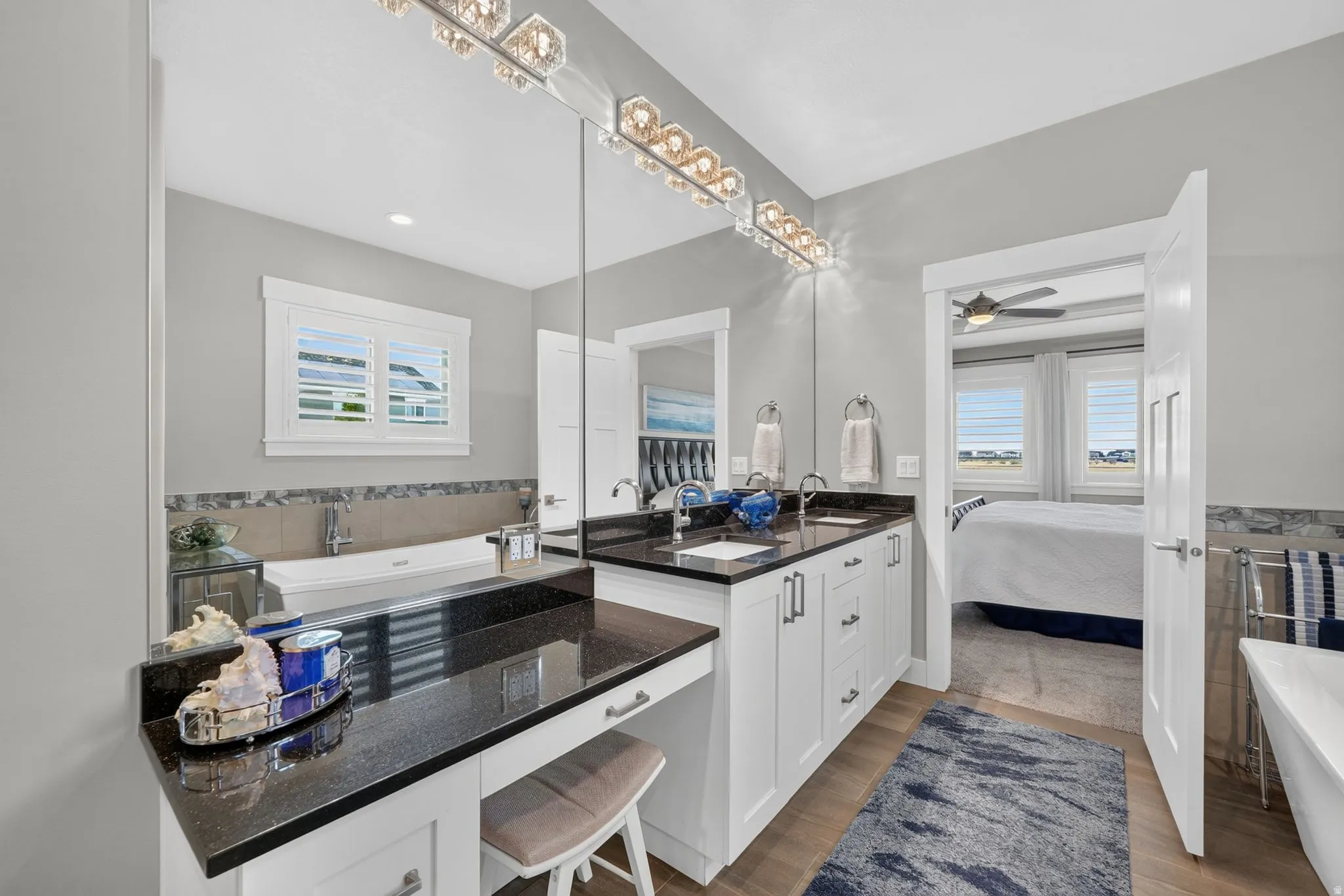 Primary bathroom featuring a large soaking tub, dual sinks, dark stone countertops, wood-finish flooring, and white cabinetry