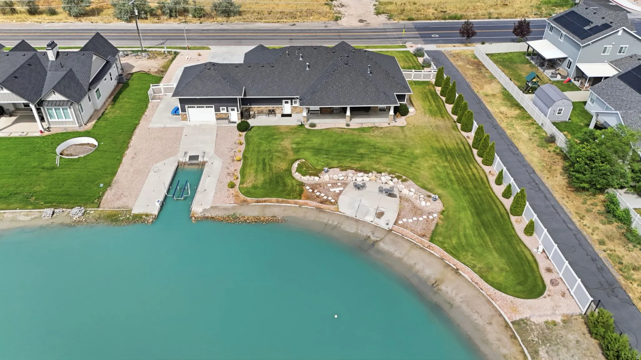 Waterfront property featuring a private boat launch, extensive manicured lawn, a concrete patio, and mature landscaping