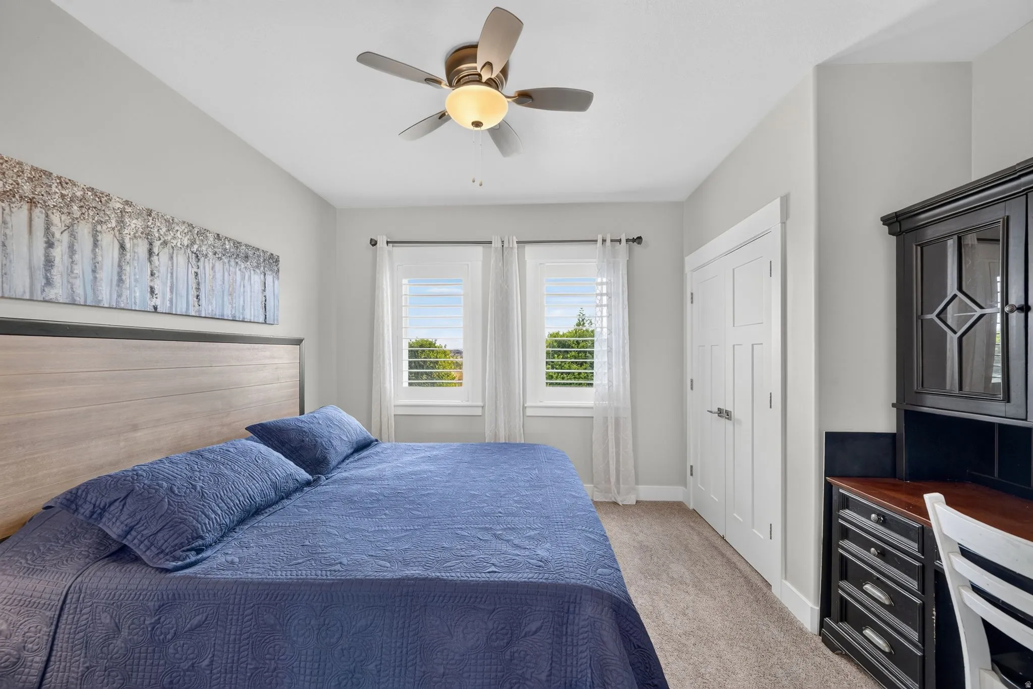 Spacious spare bedroom featuring two windows with white plantation shutters, a white paneled door, and a ceiling fan with integrated lighting