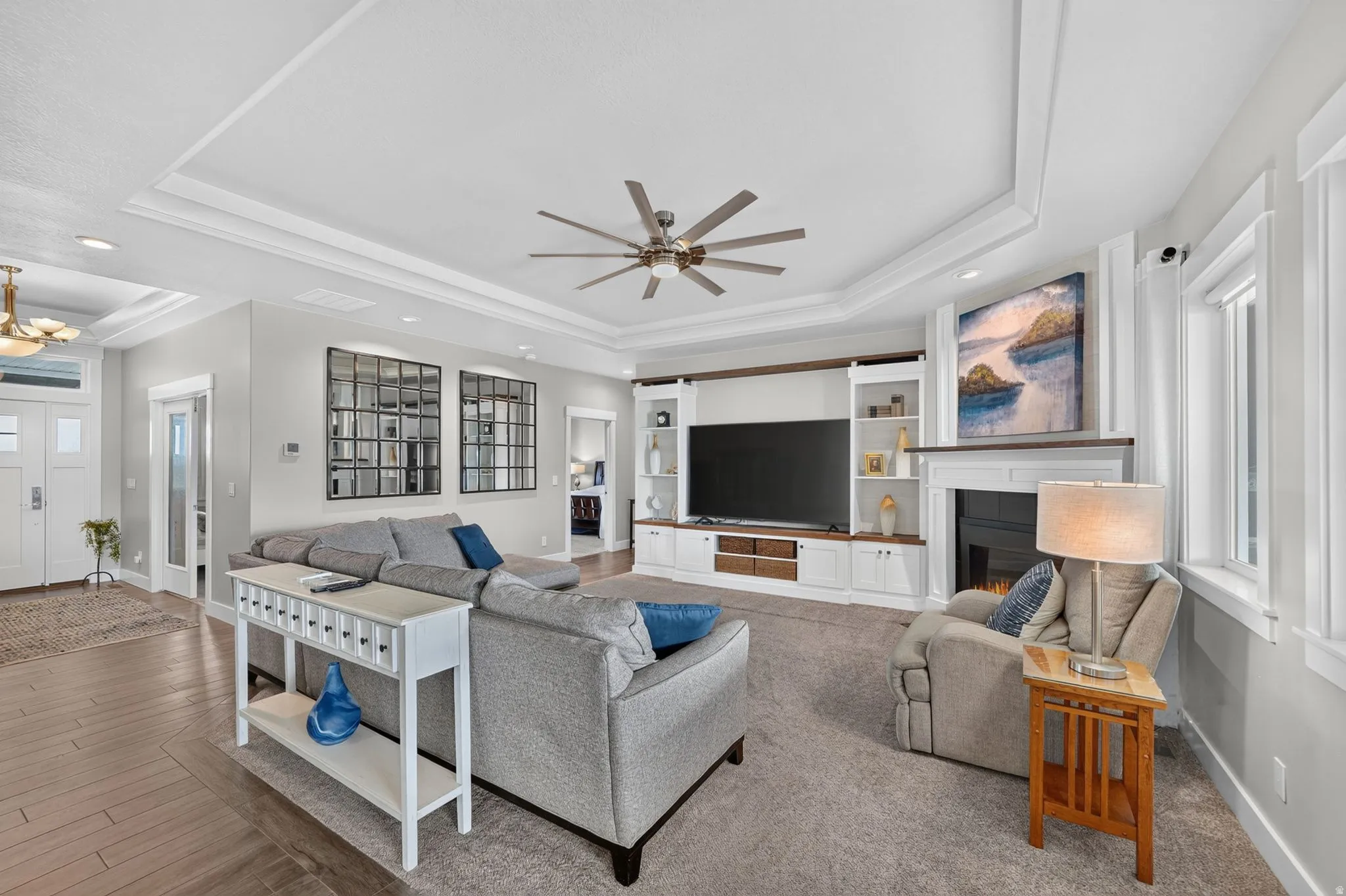 Living area featuring a tray ceiling with a ceiling fan, a built-in media center with shelving, a fireplace with a mantel, and multiple windows