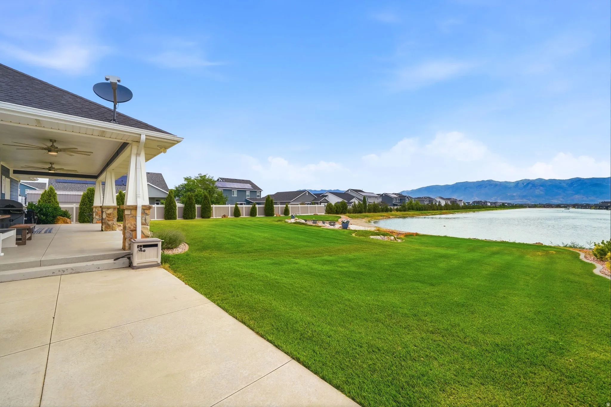 Expansive green lawn with a covered patio featuring ceiling fans and stone-clad columns