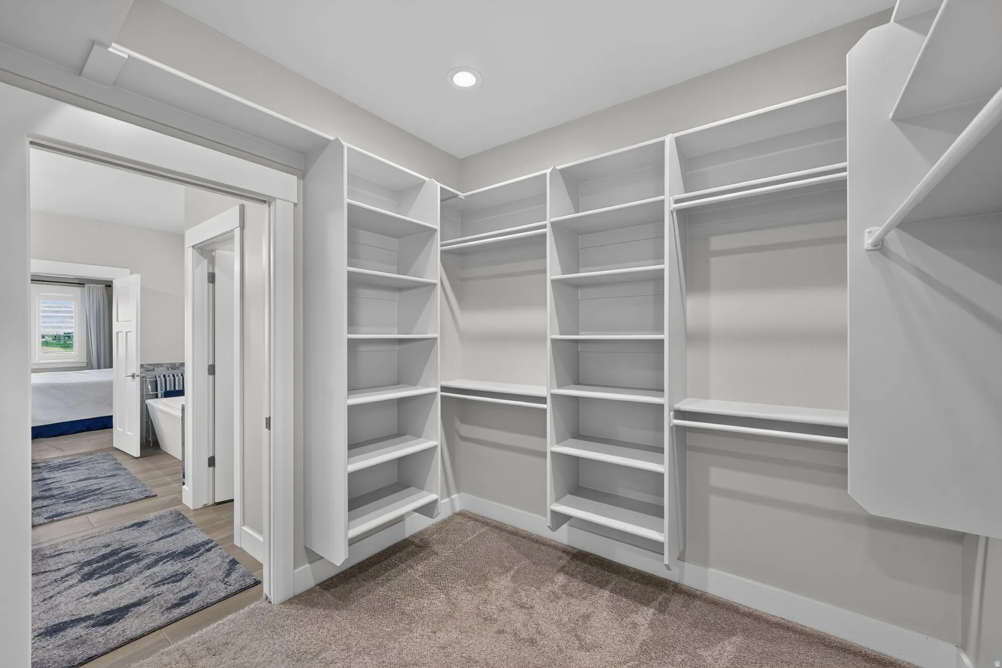 Large primary walk-in closet featuring extensive built-in shelving, multiple hanging rods, recessed lighting, and soft carpeting