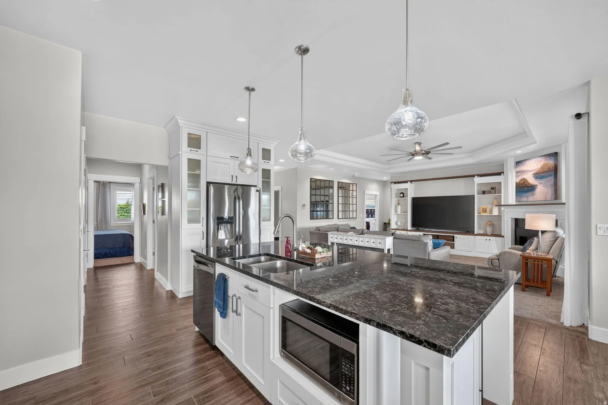 Expansive kitchen island featuring a dark speckled countertop, undermount sink, built-in microwave, and views of the living room