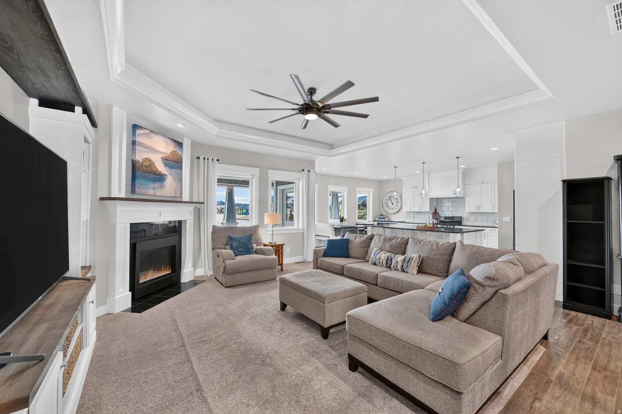 Open-concept living area featuring a fireplace with a white mantel, tray ceiling, recessed lighting, and a contemporary ceiling fan