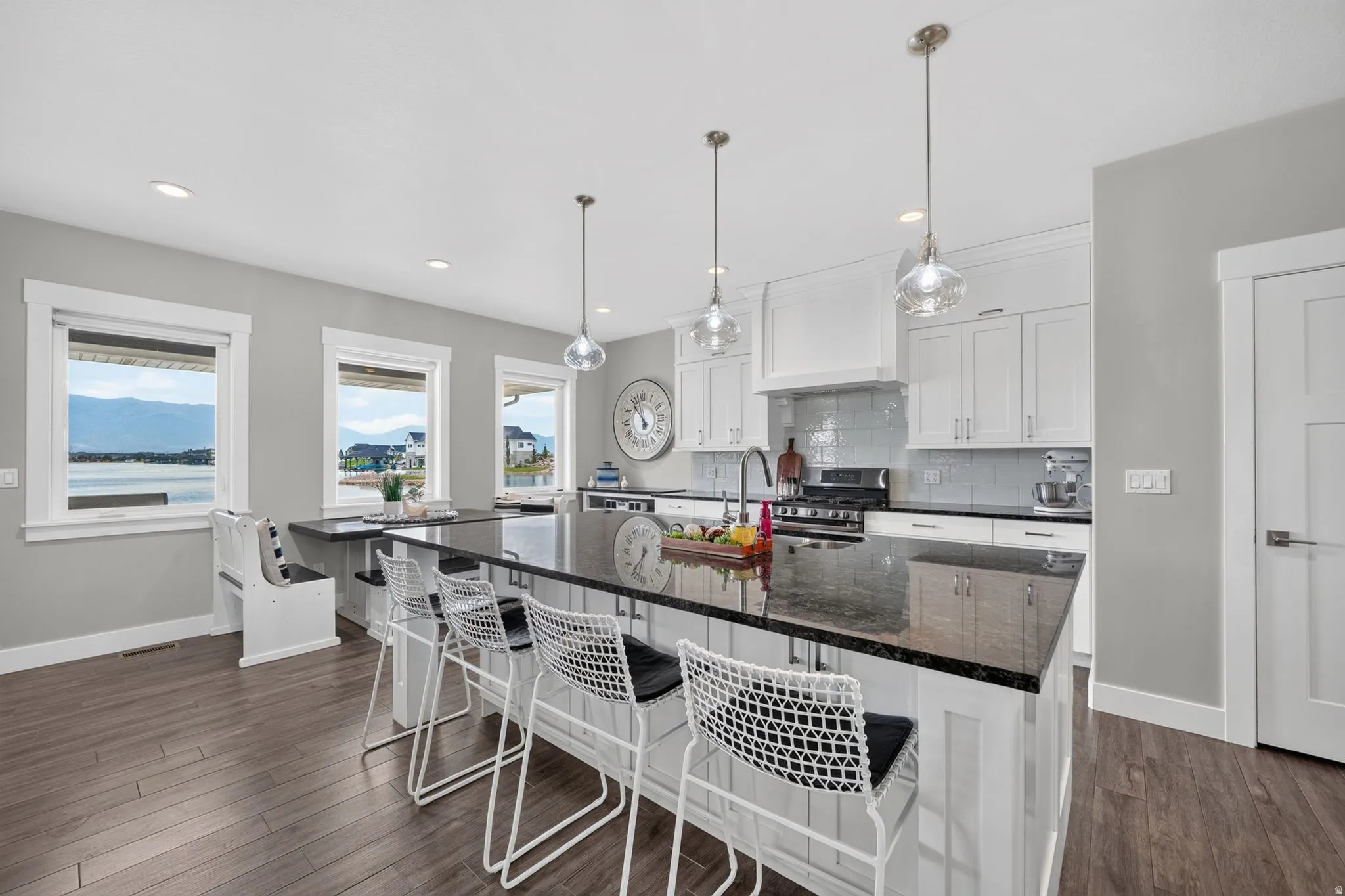 Modern kitchen featuring a large island with dark stone countertop, white shaker cabinetry, stainless steel range, and wood-finish flooring