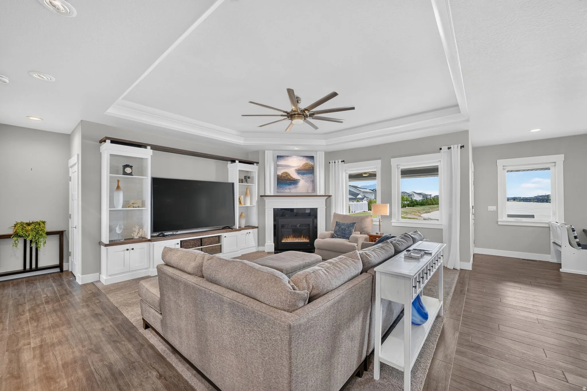 Spacious living area featuring wood-finish flooring, an illuminated corner fireplace, and a built-in entertainment center with shelving and storage