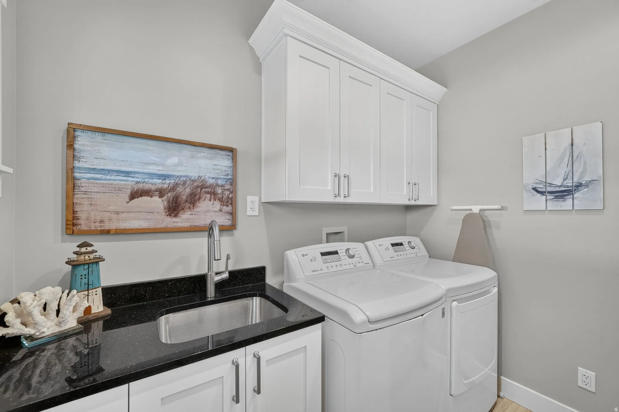 Dedicated laundry space featuring white shaker-style cabinetry, a dark countertop with an undermount stainless steel sink, and a chrome pull-down faucet