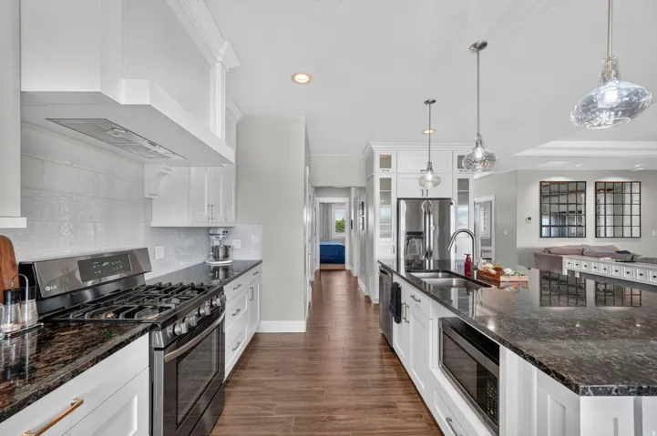 Modern kitchen featuring white cabinetry, dark granite countertops, stainless steel appliances, and a tiled backsplash