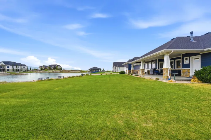 Expansive green lawn bordering a water feature, with a covered patio featuring stone-clad pillars and dark siding