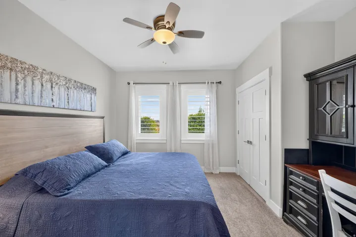 Spacious spare bedroom featuring two windows with white plantation shutters, a white paneled door, and a ceiling fan with integrated lighting