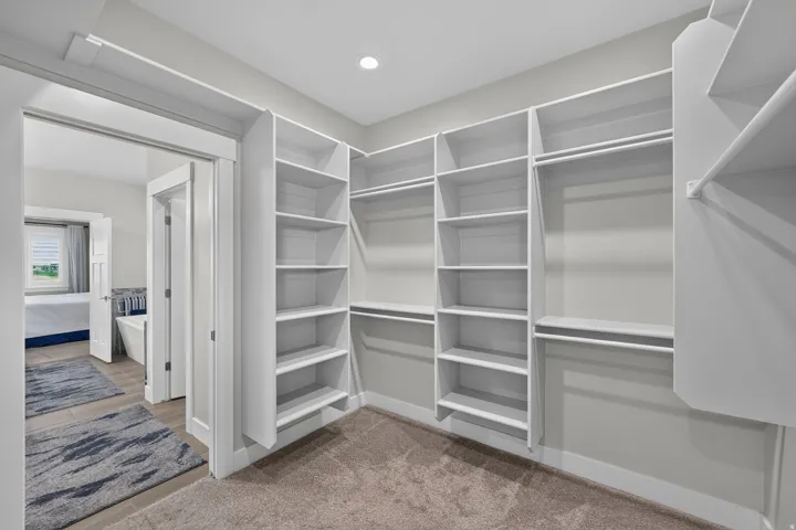 Large primary walk-in closet featuring extensive built-in shelving, multiple hanging rods, recessed lighting, and soft carpeting