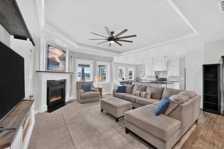 Open-concept living area featuring a fireplace with a white mantel, tray ceiling, recessed lighting, and a contemporary ceiling fan
