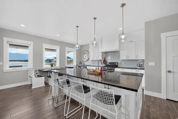 Modern kitchen featuring a large island with dark stone countertop, white shaker cabinetry, stainless steel range, and wood-finish flooring