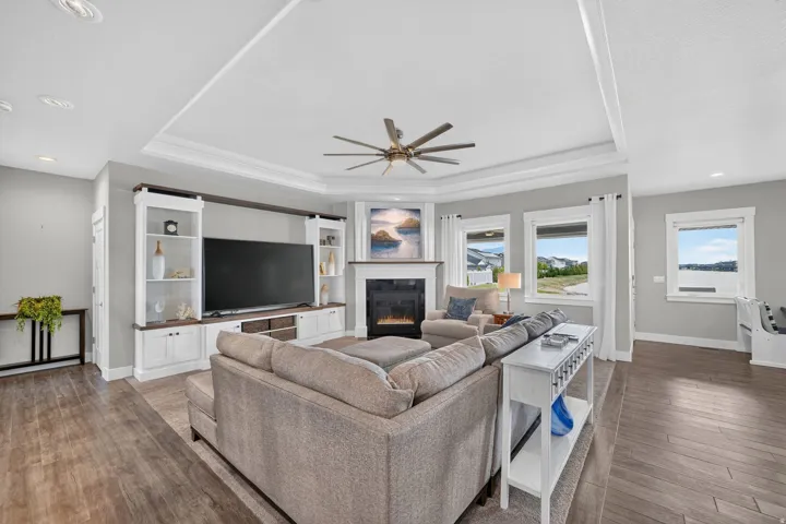 Spacious living area featuring wood-finish flooring, an illuminated corner fireplace, and a built-in entertainment center with shelving and storage