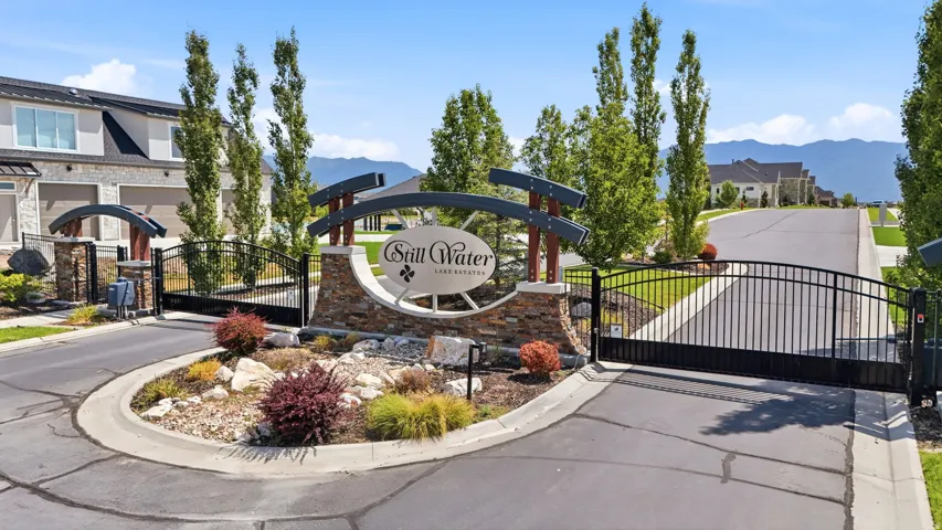 Gated community entry featuring a stone and metal sign, black wrought iron gates, and established landscaping