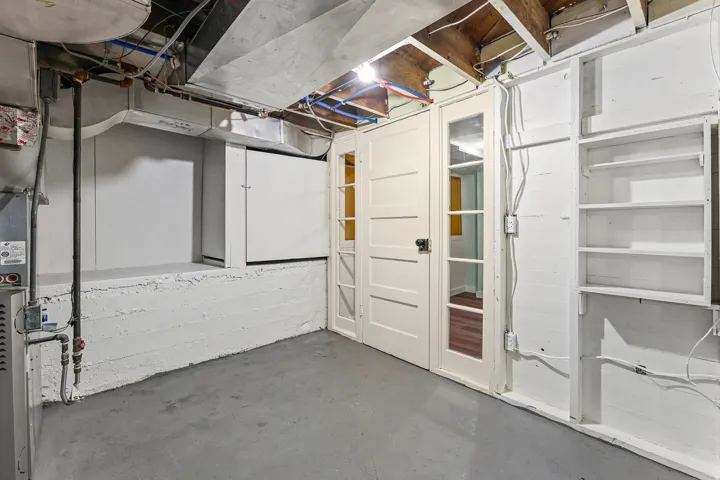 Unfinished basement area featuring painted concrete walls, exposed ceiling joists, and a concrete floor