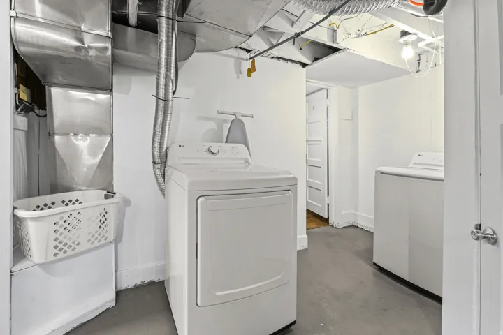 Dedicated laundry area featuring a white washer and dryer set, exposed ceiling ductwork, and painted concrete flooring