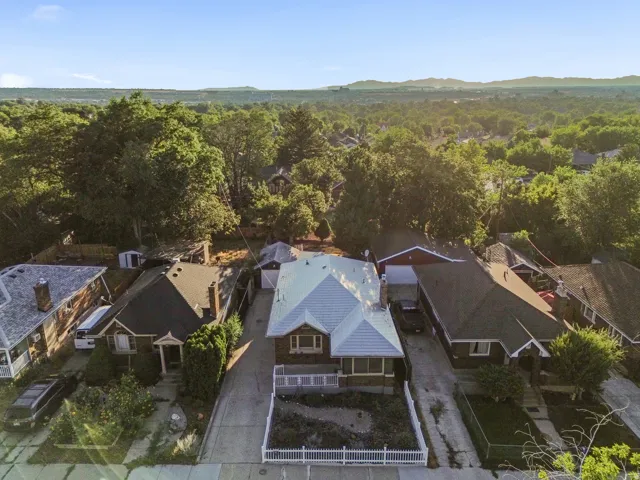 Aerial perspective showcasing a property featuring a white picket fence, a light-colored roof, and mature perimeter trees